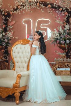 A teenage girl celebrates her quinceañera in a beautifully decorated room with flowers.