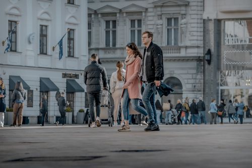 Free Couple walking in a busy European town square, showcasing city life and fashion. Stock Photo