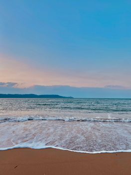 Calm evening waves touch the sandy shore at Les Sables-d'Olonne, France, under a vibrant sunset.