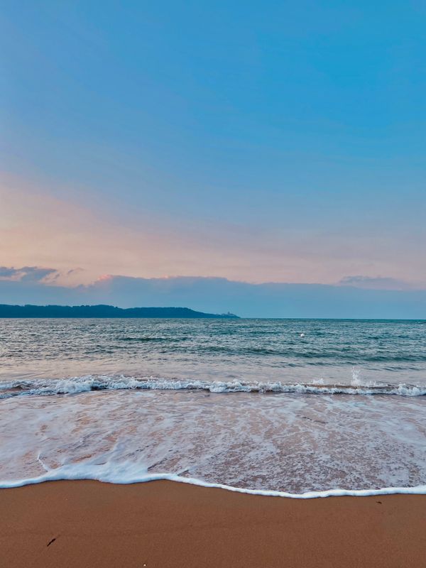 As ondas calmas da tarde tocam a areia na praia de Les Sables-d'Olonne, França, sob um vibrante pôr do sol.