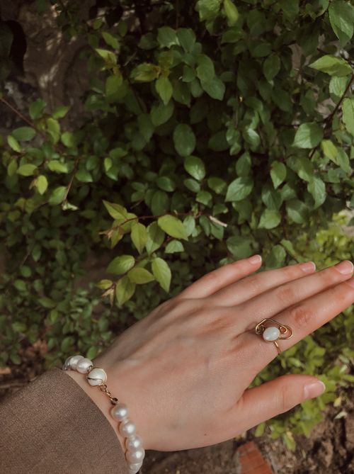 Free Close-up of a woman's hand wearing pearl jewelry against lush green foliage. Stock Photo