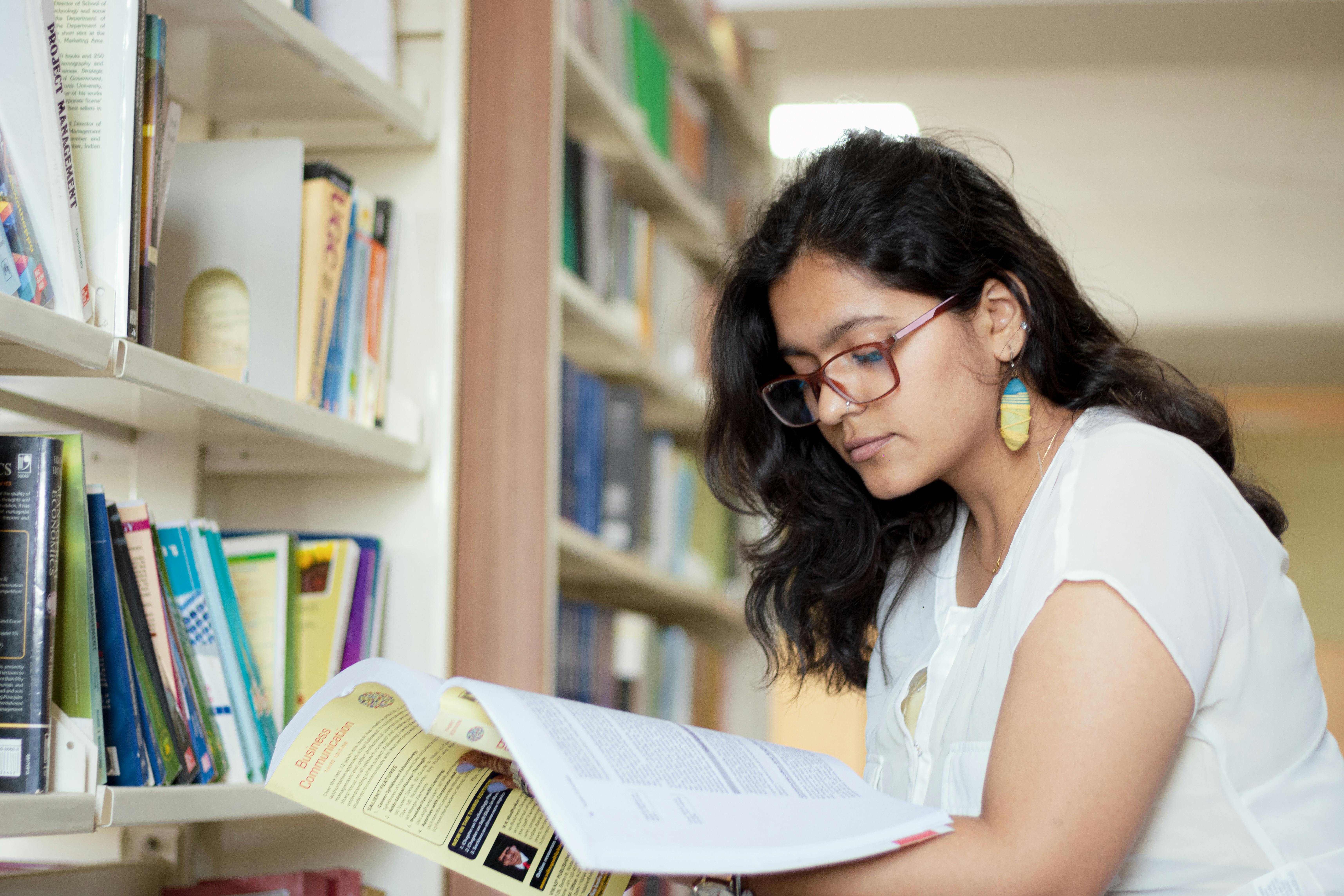 portrait of a smiling young indian student reading a book in a library