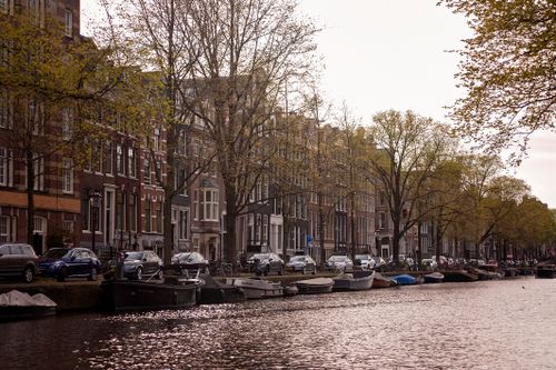 Free Peaceful view of Amsterdam canal with boats, trees, and historic architecture during spring. Stock Photo