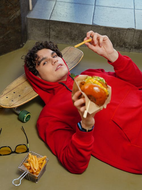 A Young Man with a Skateboard Holding a Burger