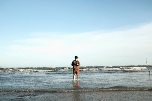 Free A young man stands in shallow ocean waters under a clear blue sky. Stock Photo