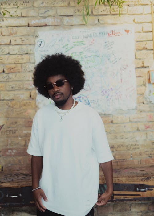 Young Man in a White T-shirt and Sunglasses Standing on the Background of a Wall 