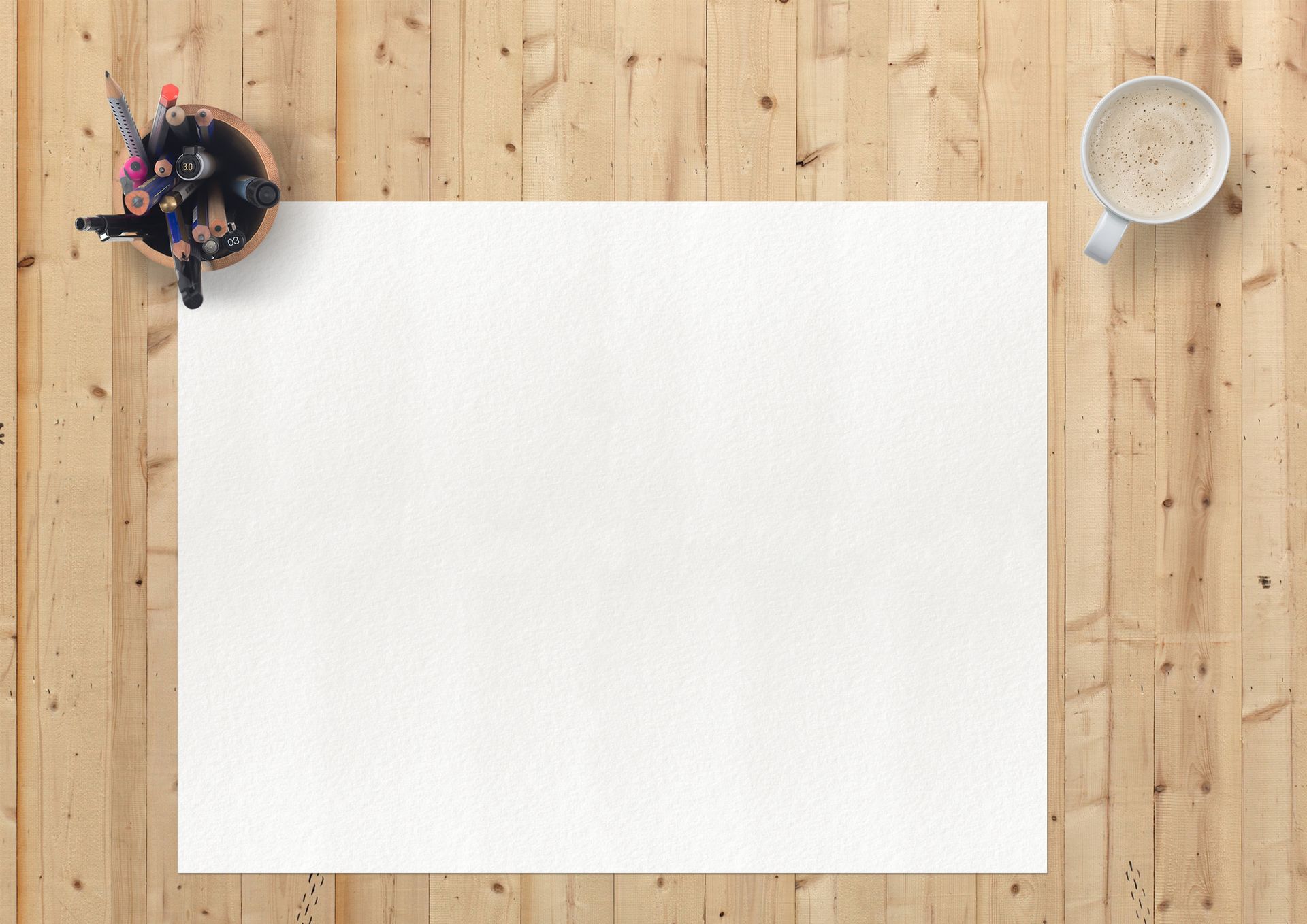 Flat lay of art supplies, blank paper, and coffee on a wooden desk for a creative workspace.