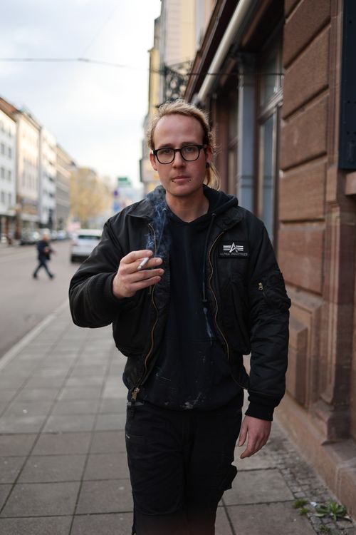 Free Stylish man with eyeglasses smoking on a city sidewalk, showcasing urban fashion. Stock Photo