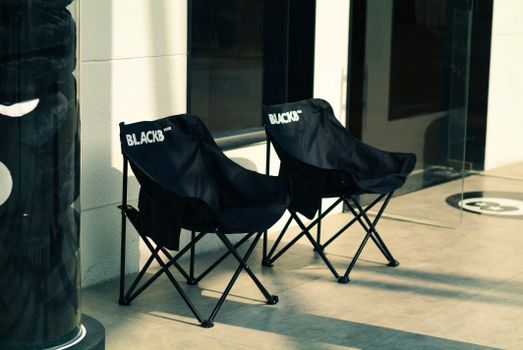 Two black foldable chairs placed outside a modern glass entrance, ideal for commercial use.