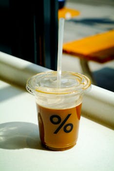 Close-up of an iced coffee with a straw on a sunny outdoor table, perfect for summer vibes.