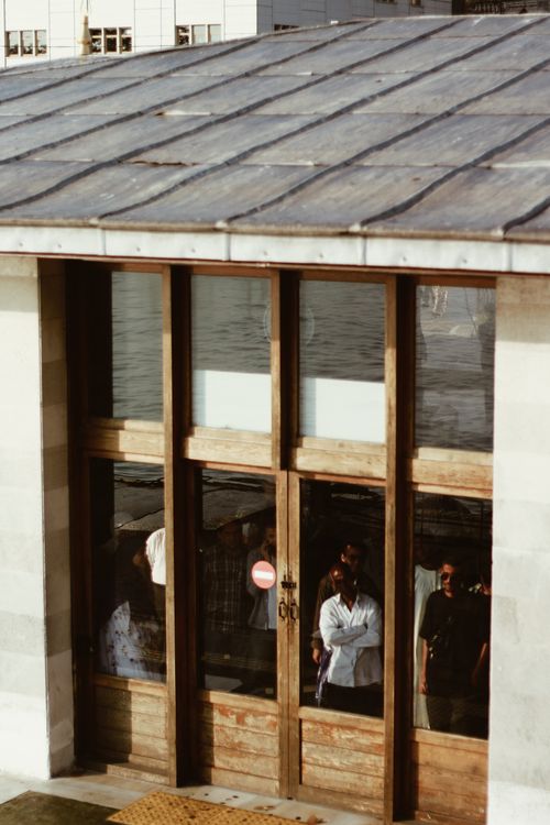 Free People standing and visible through glass windows of a rustic building with wooden doors. Stock Photo