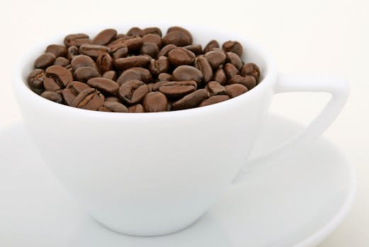 A white cup filled with roasted coffee beans, perfect for caffeine themes.