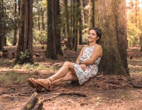 Woman Wearing a Dress with a Floral Pattern Sitting in a Forest 
