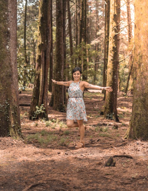 Woman Wearing a Dress with a Floral Pattern Standing in a Forest 