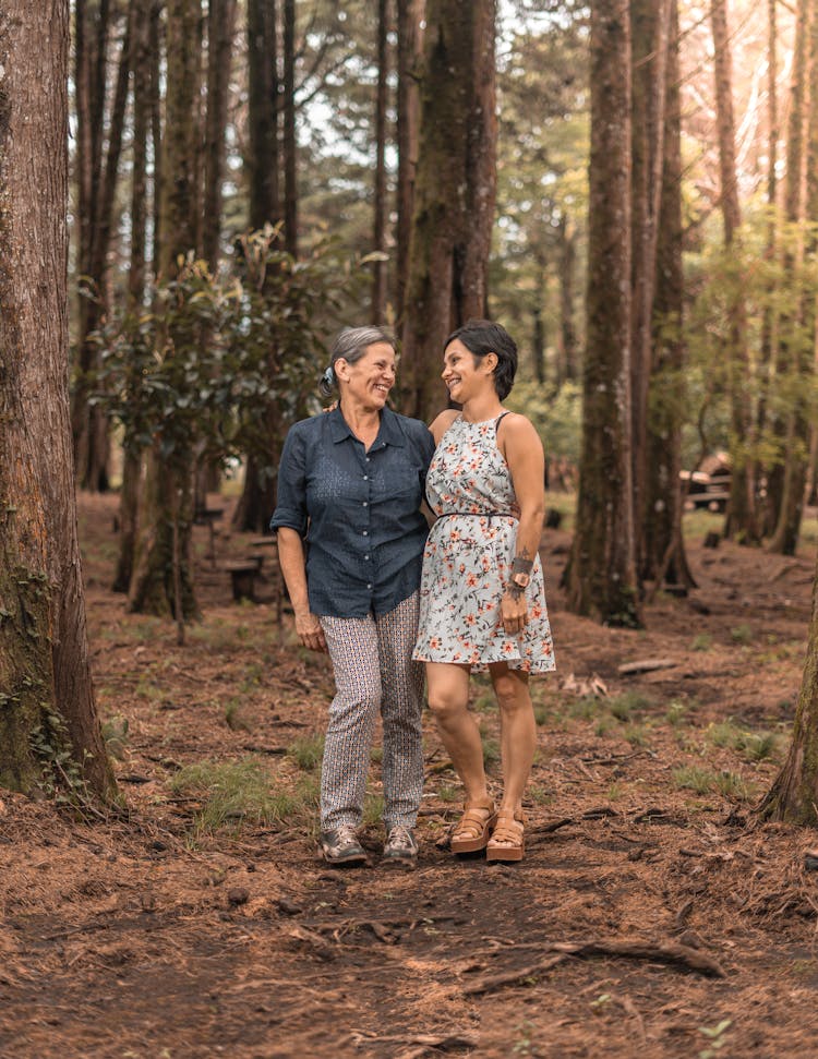 Woman With Gray Hair And Her Adult Daughter Standing Together In A Forest And Smiling 