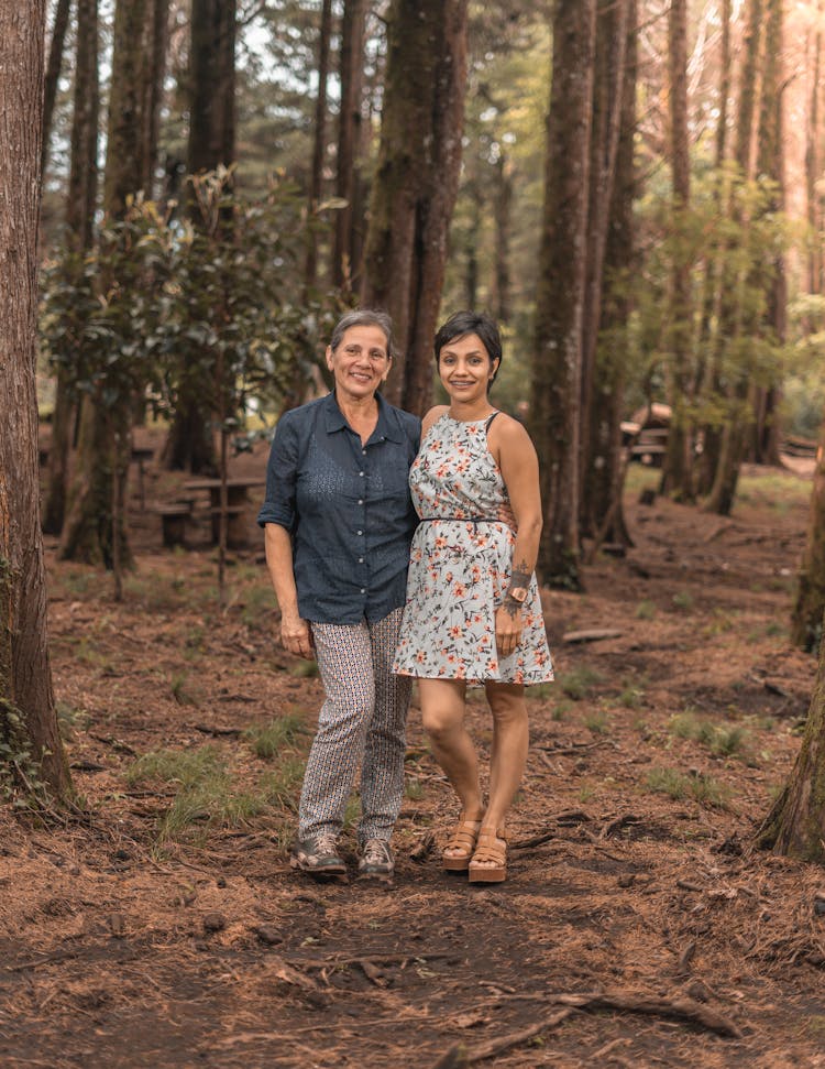 Woman With Gray Hair And Her Adult Daughter Standing Together In A Forest And Smiling 