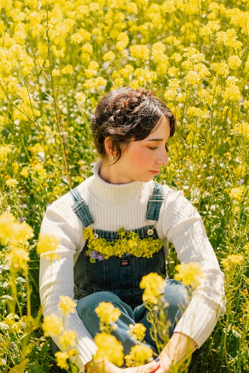 黄色い花畑に座っているデニム ダンガリーの女性