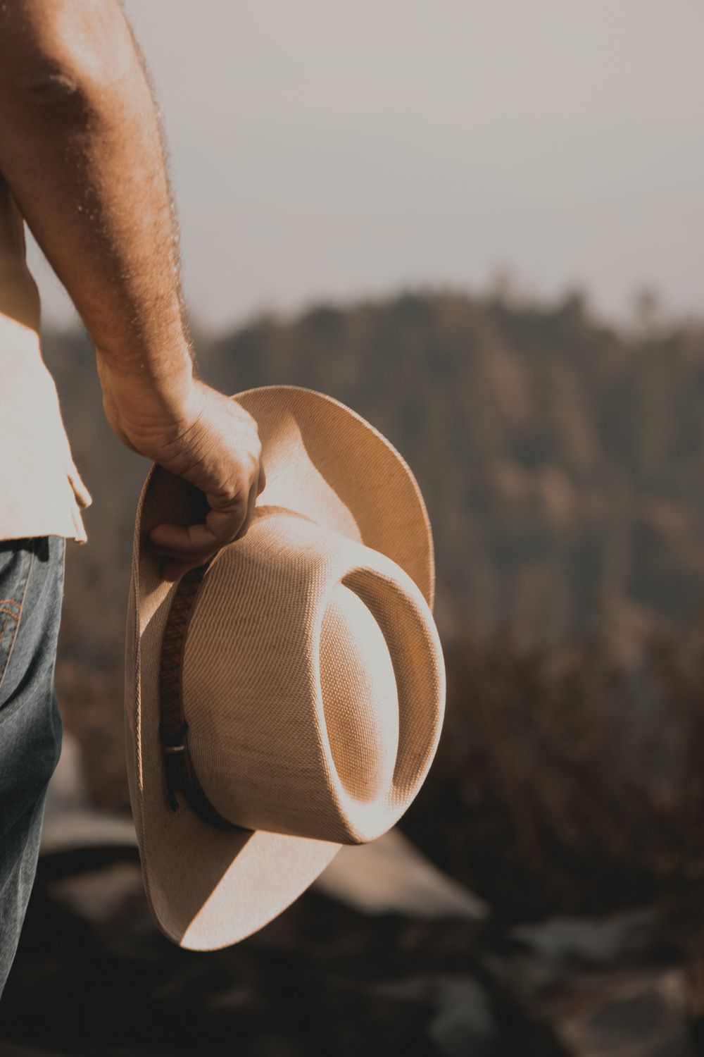 A hand holding the brim of a western hat outdoors