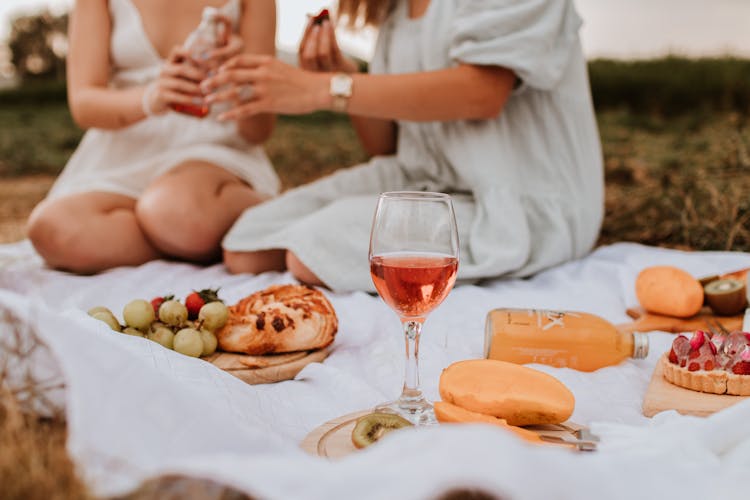 Food On A Picnic Blanket With Two Women Sitting In The Background