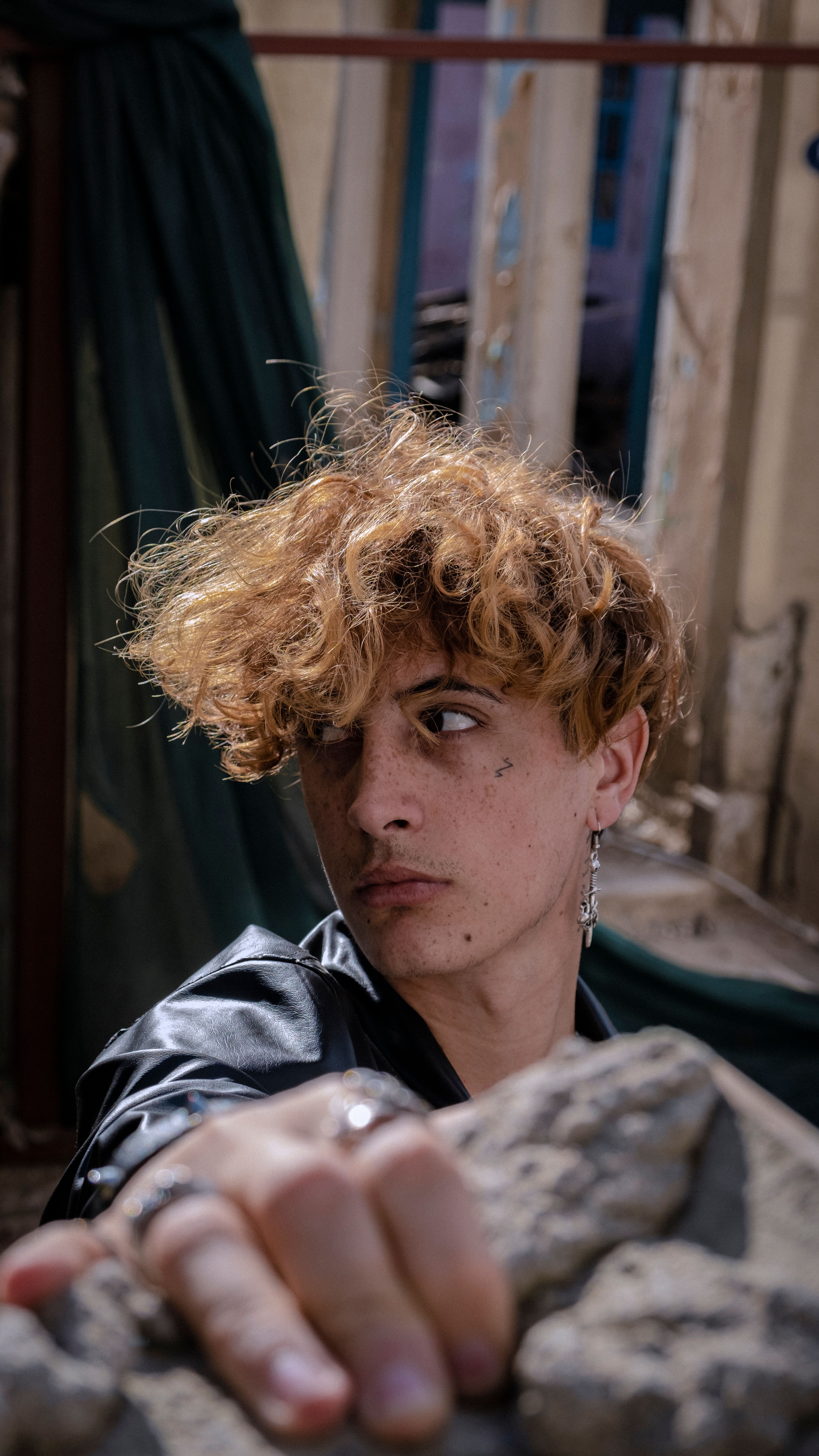Portrait of a young man with curly hair, posing dramatically in an urban environment.