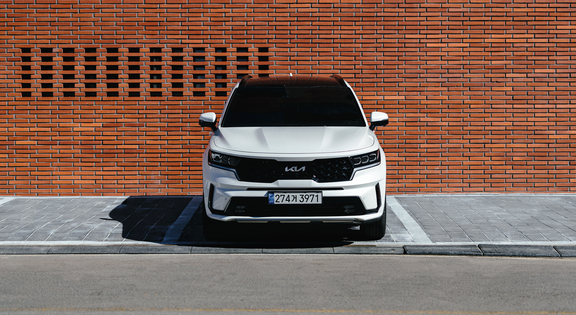 A sleek white SUV parked against a red brick wall in an urban setting during the day.