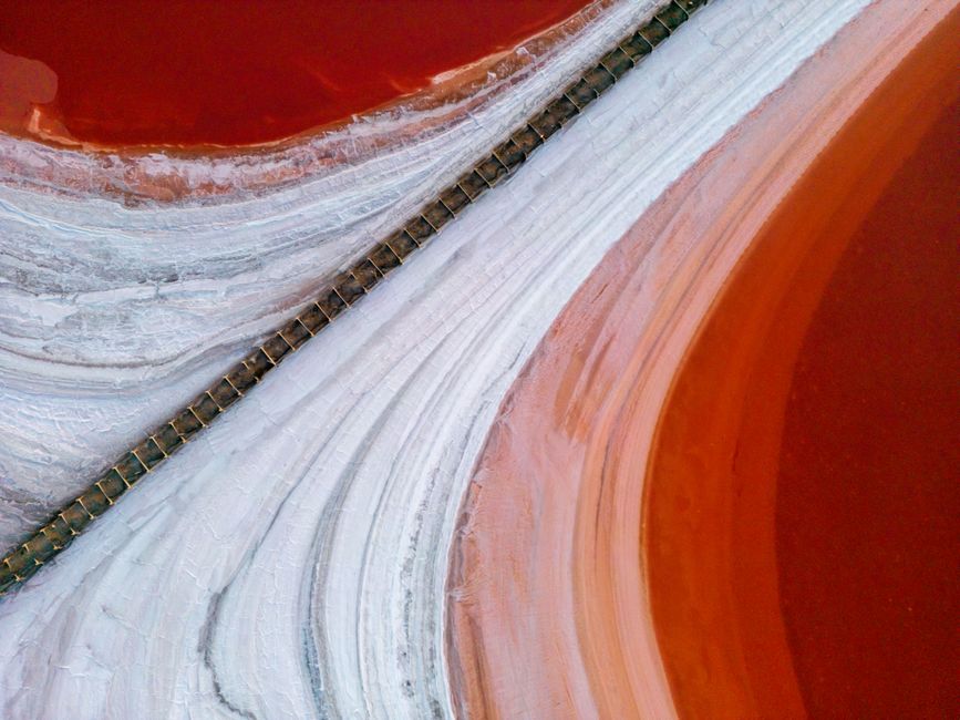 Aerial photograph showcasing the vivid colors of a pink salt lake with a railway crossing through it.