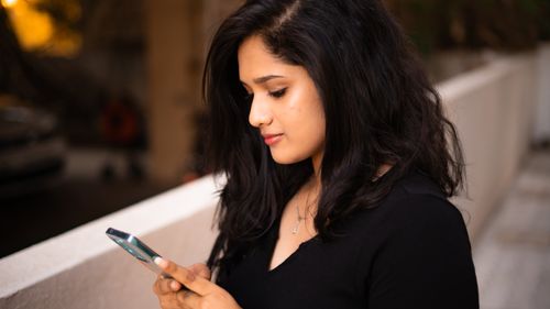 Free A young woman with black hair engages with her smartphone outdoors. Calm and focused. Stock Photo