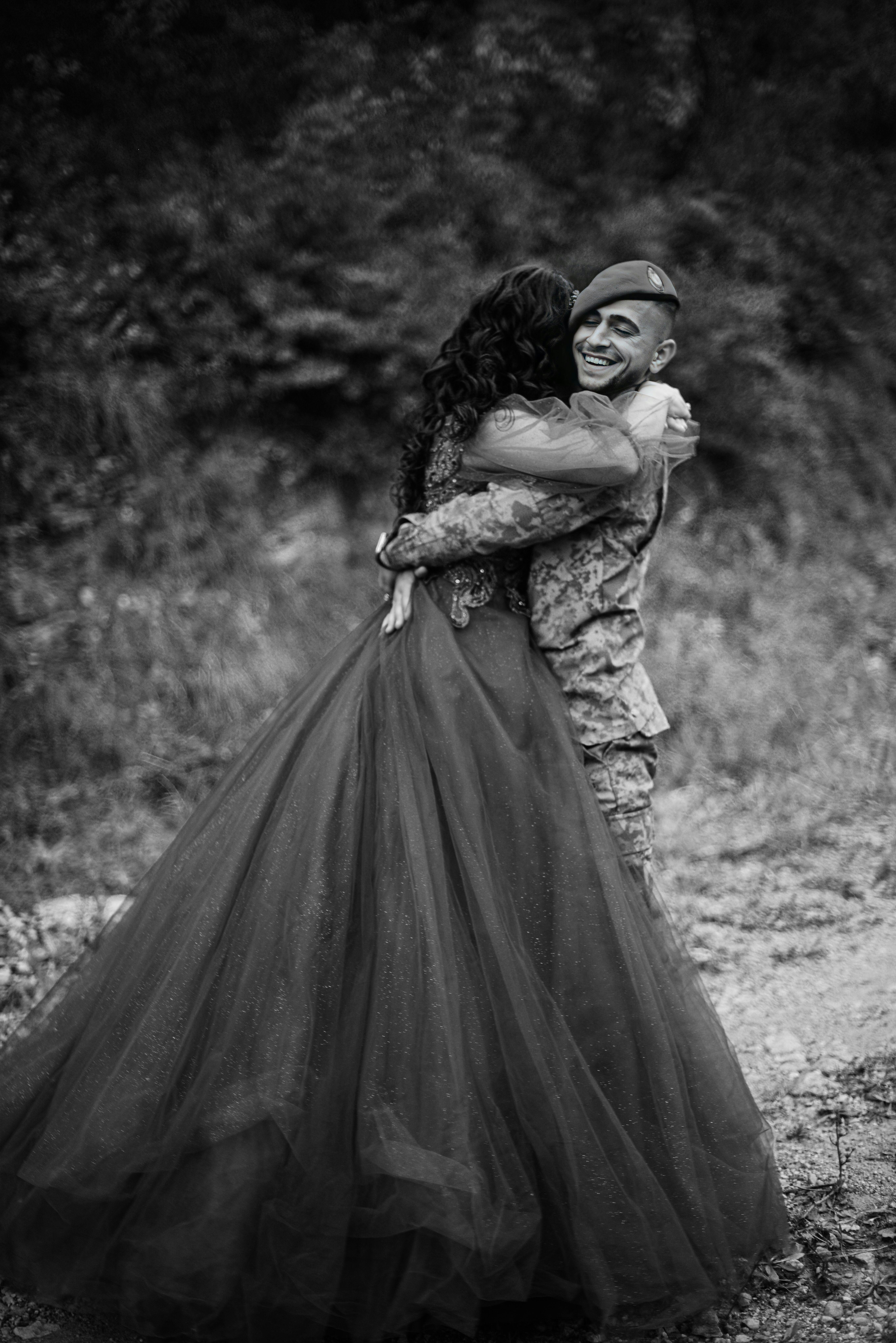 Black and white photo of a soldier embracing their partner in an evening gown outdoors.
