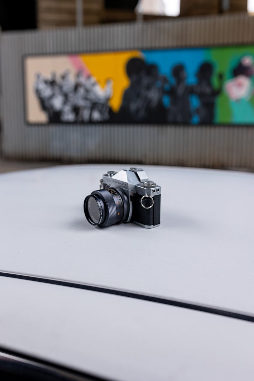 A classic vintage camera placed on a car roof, capturing an urban art background.
