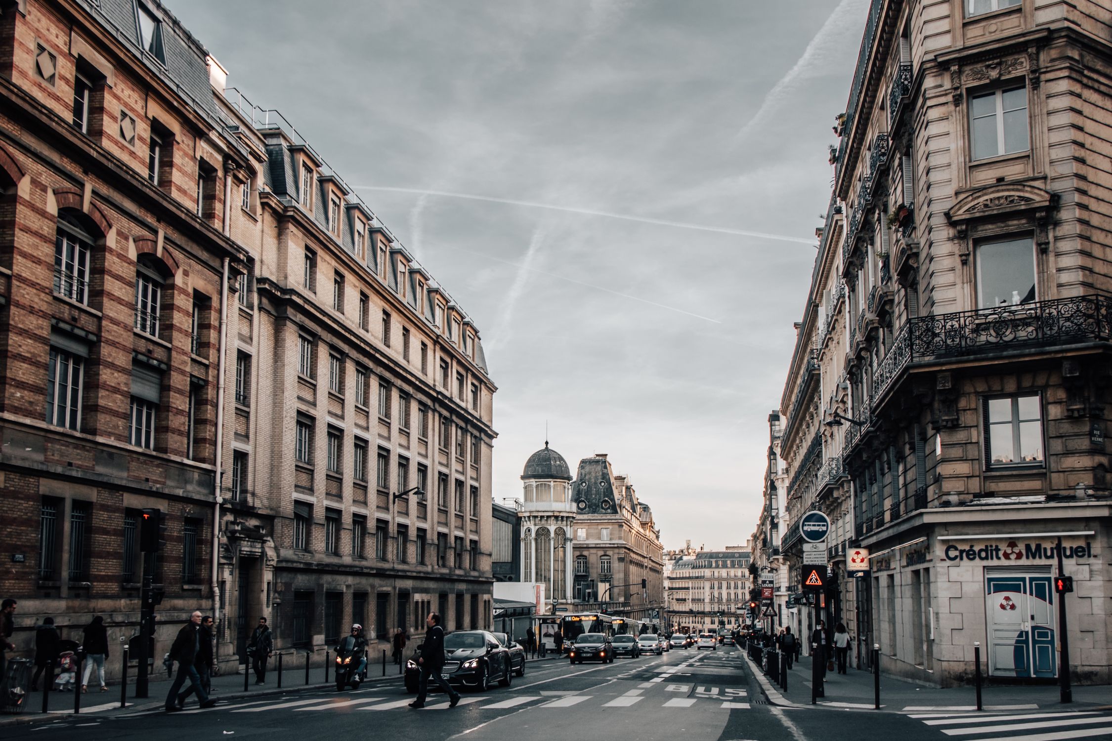 Urban street scene in Paris with classic architecture, cars, and pedestrians on an overcast day