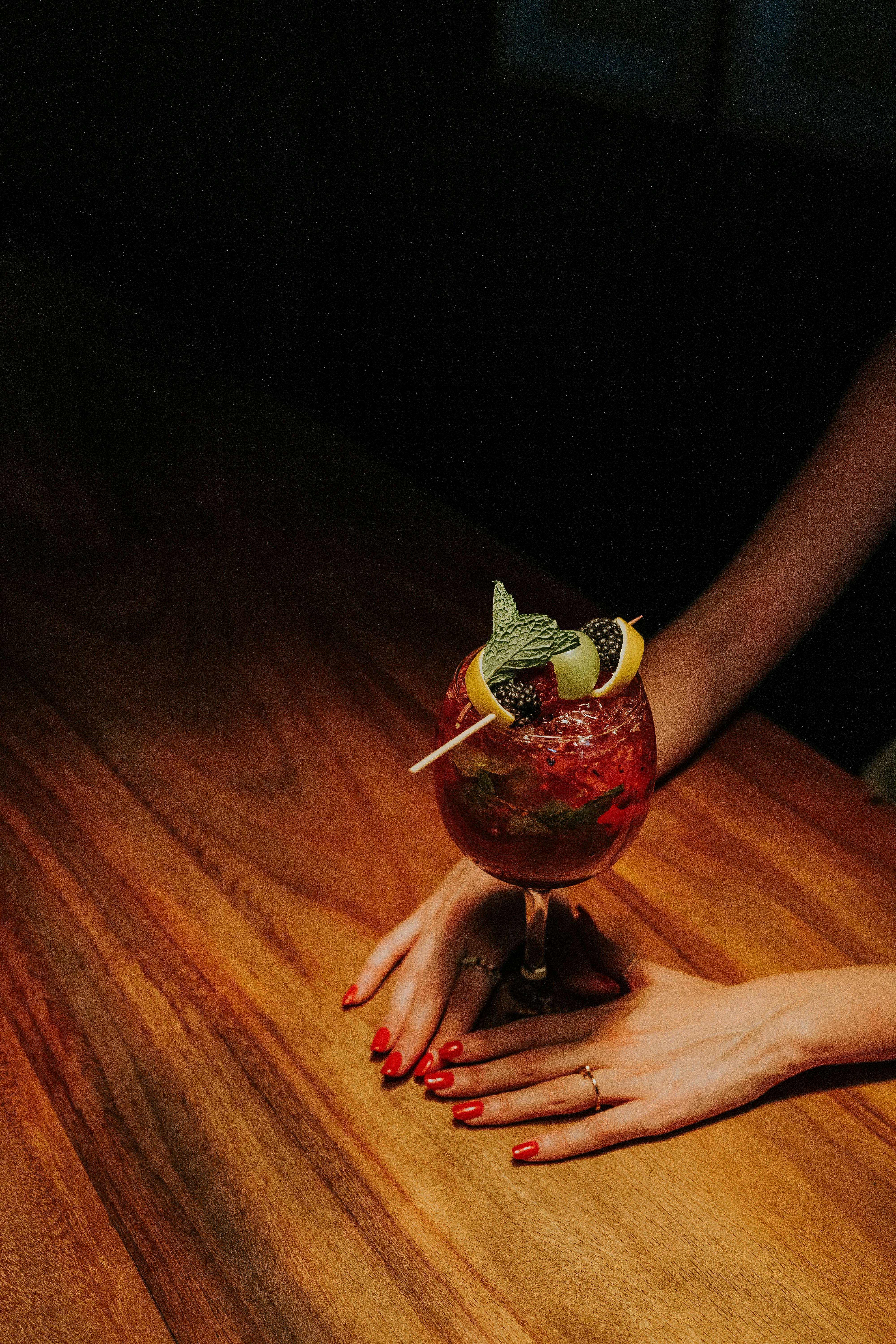 A sophisticated cocktail garnished with herbs and citrus on a wooden bar table at night.