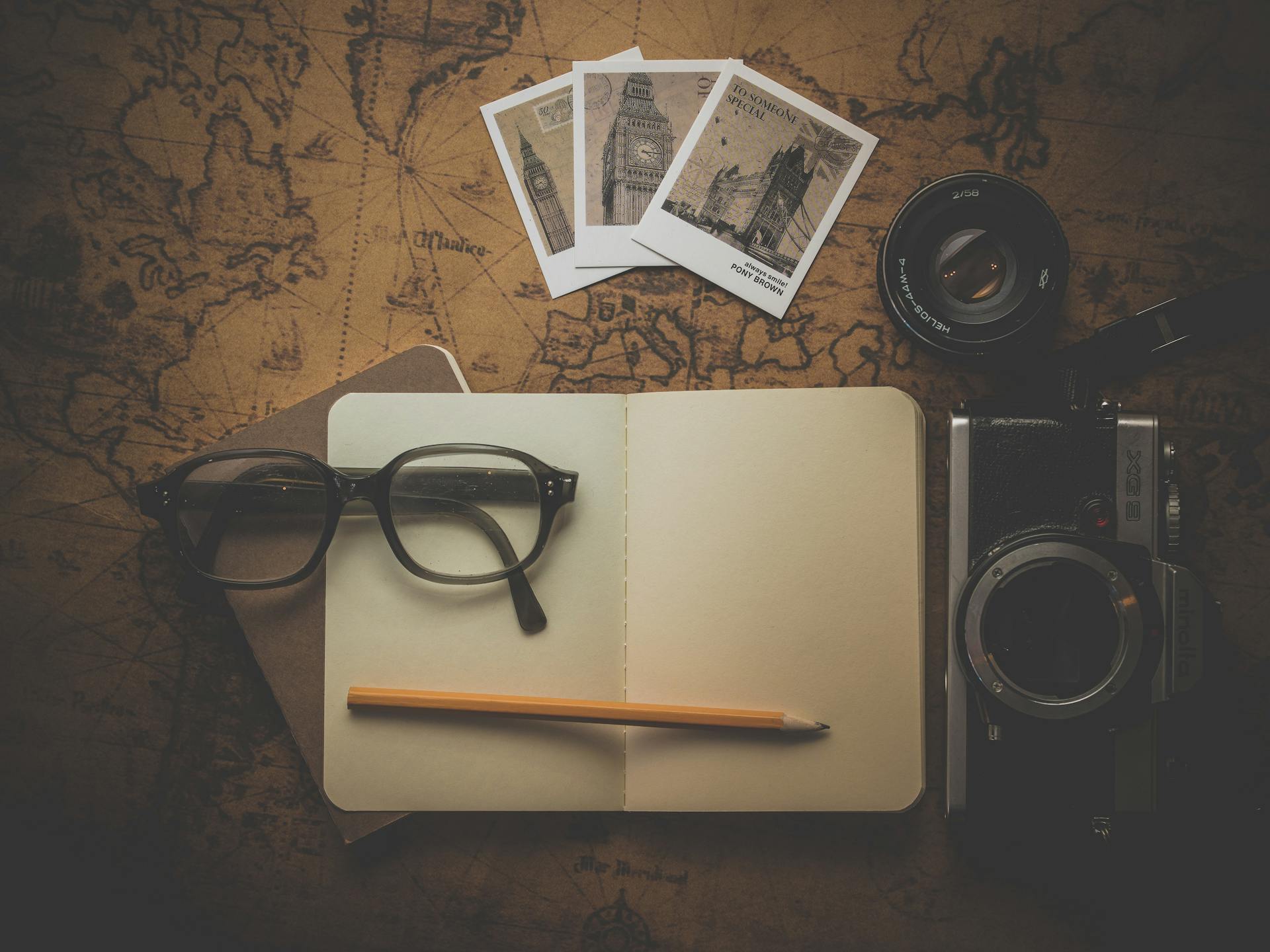 Flat lay of travel essentials including camera, notebook, eyeglasses, and map for adventure planning.