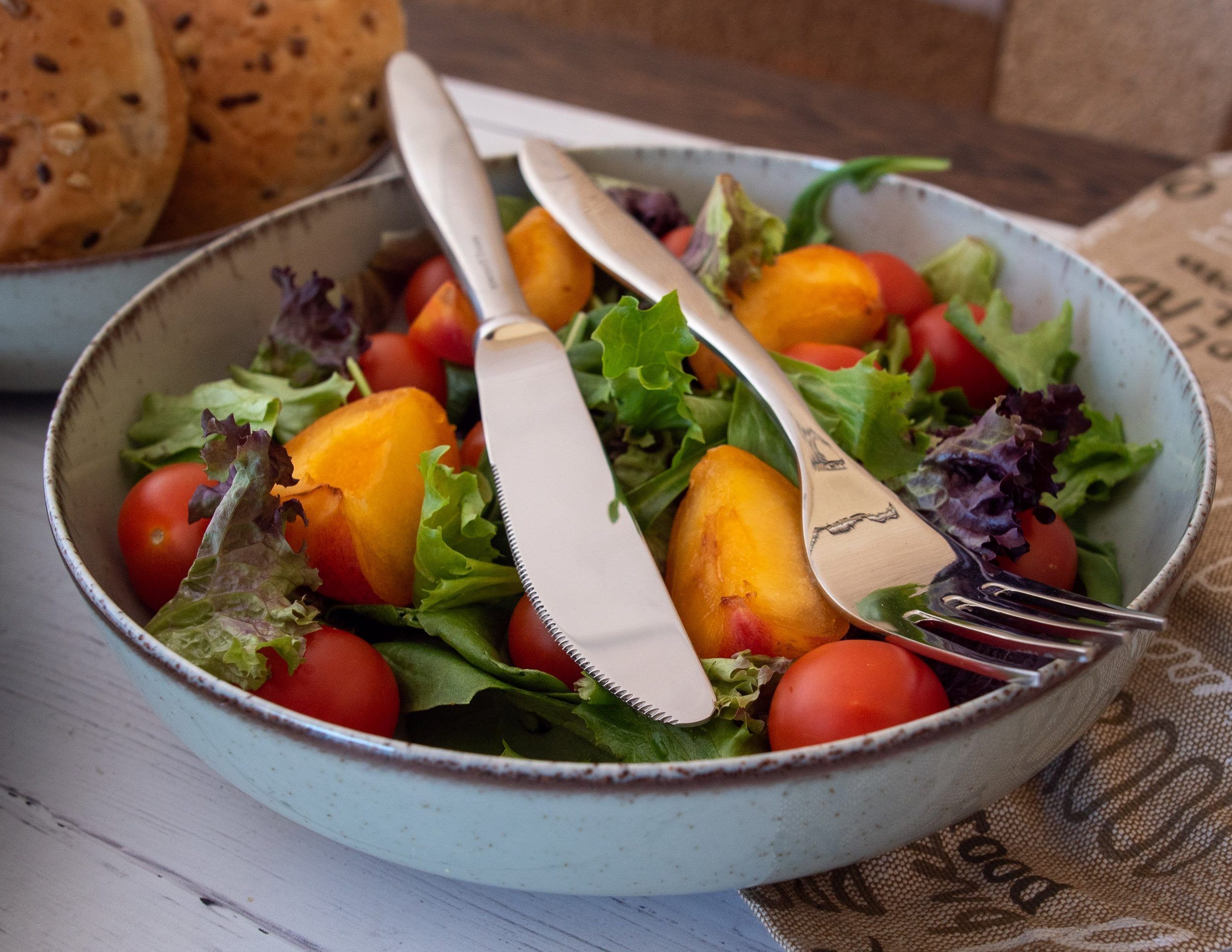 A vibrant salad featuring fresh peaches, greens, and cherry tomatoes in a ceramic bowl.
