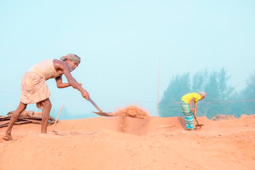 Photo of Two People Working with Shovels in the Sand