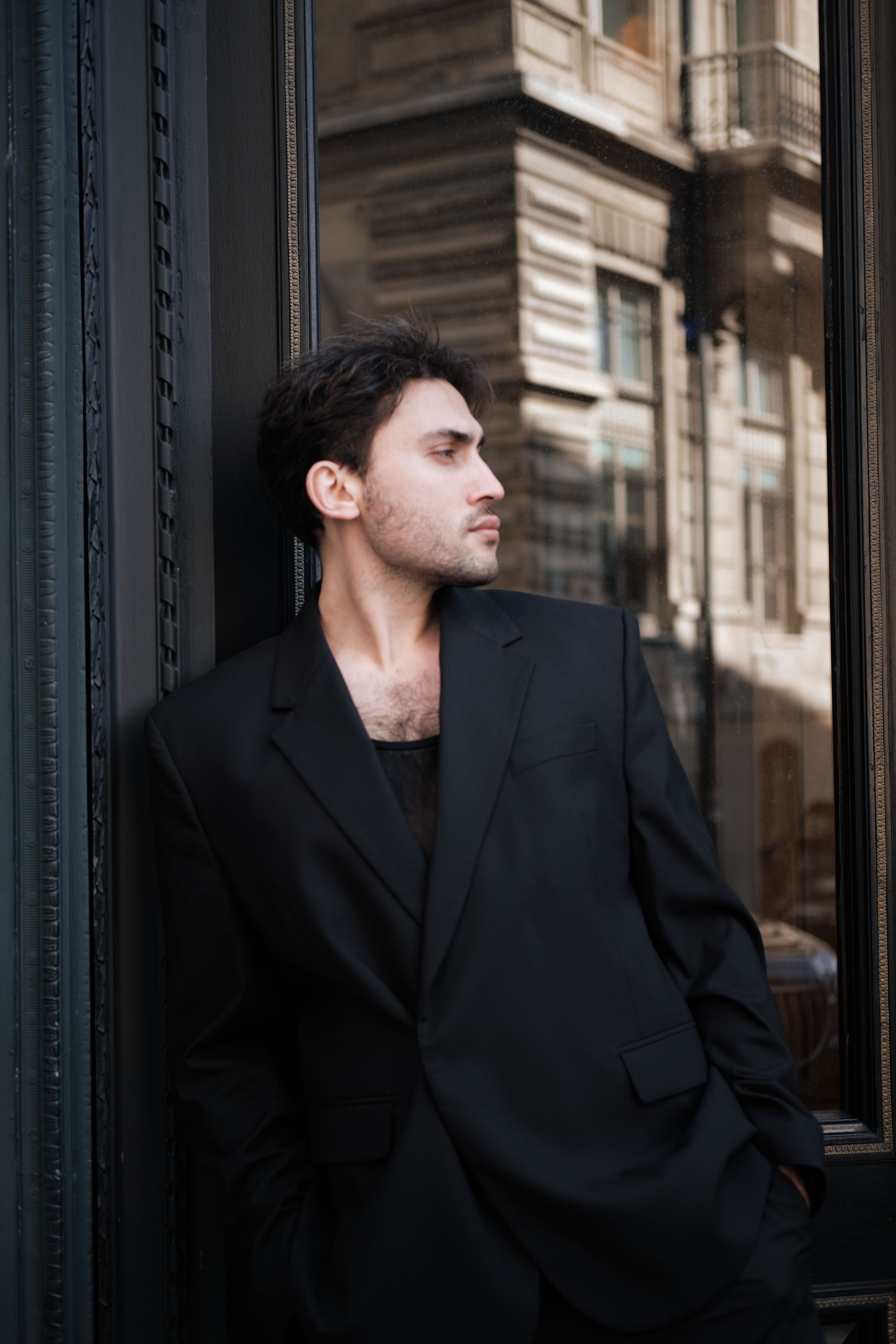 Sophisticated urban fashion portrait of a man in a black suit against a city backdrop.