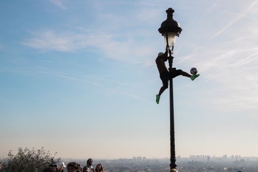 Silhouette of a man performing football tricks on a lamppost in Paris, with cityscape in the background.