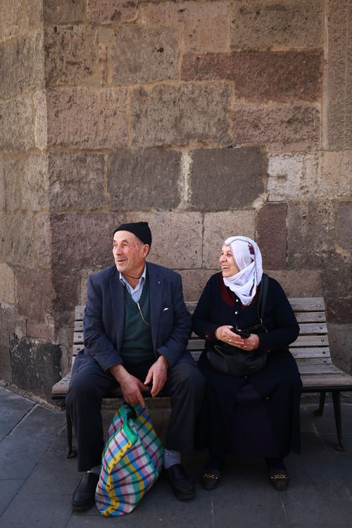 Free An elderly couple sits outdoors, smiling and enjoying each other's company on a city bench. Stock Photo