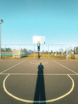 Shadow cast on an empty basketball court under a clear blue sky, creating a serene urban scene.