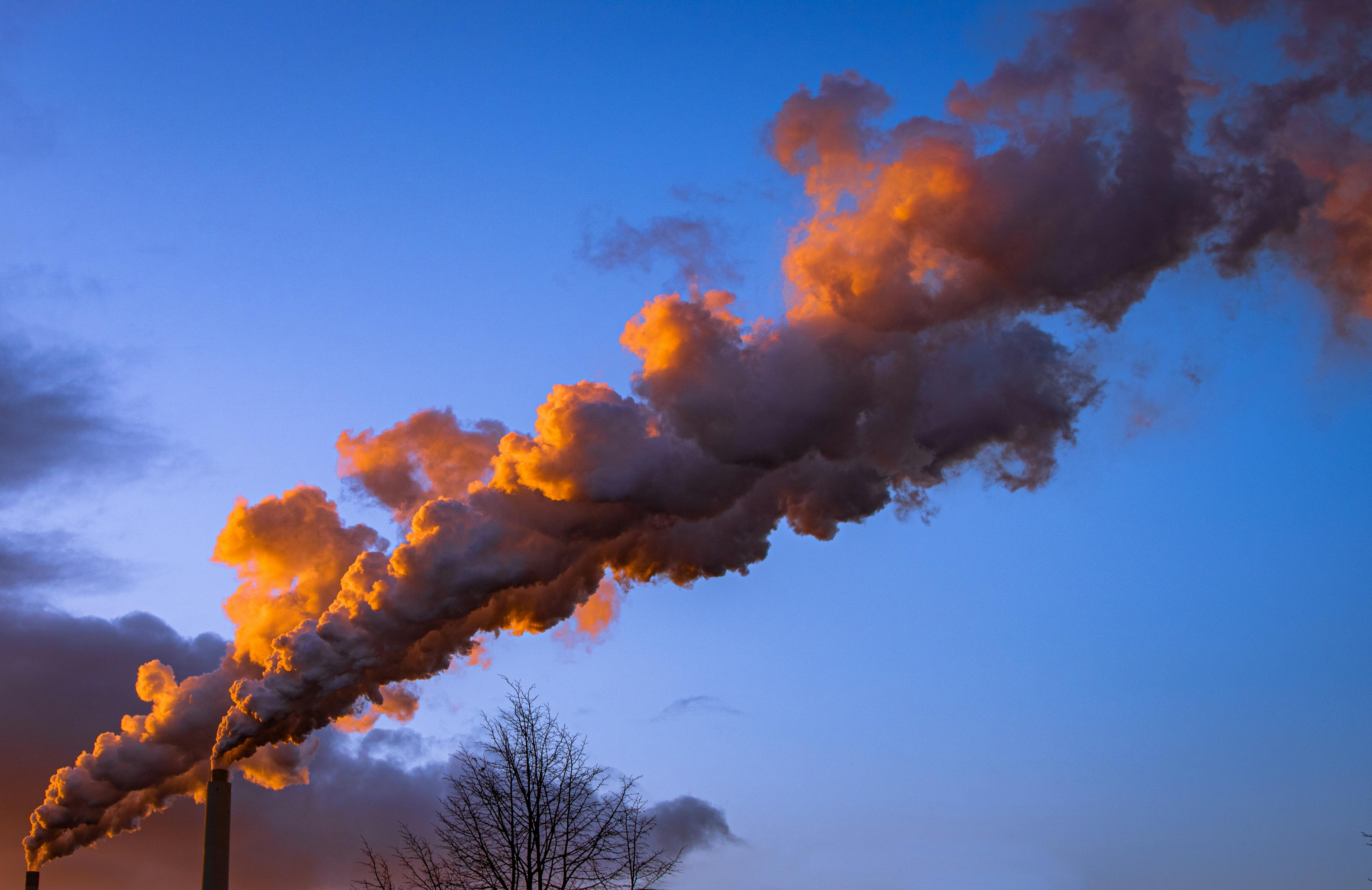 Industrial smokestack releasing orange-hued smoke during sunset against a vibrant sky.