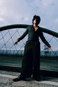 Man striking a pose on a bridge at sunset, showcasing urban fashion and style.