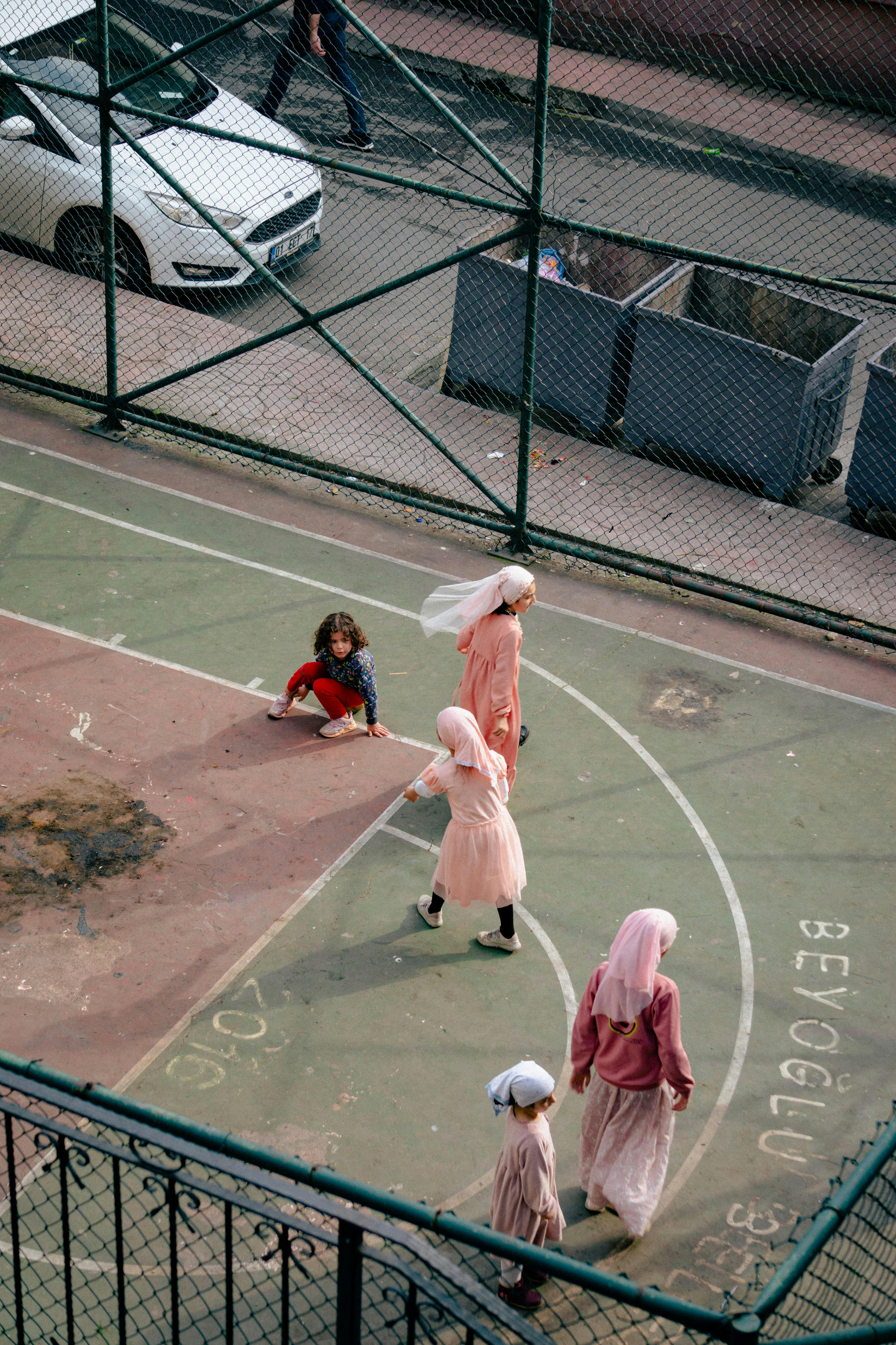Children in hijabs playing on a city basketball court, showcasing urban life and diversity.