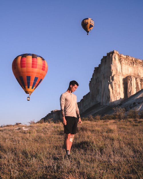Man Standing on Field with Hot Air Balloons Flying in Background 