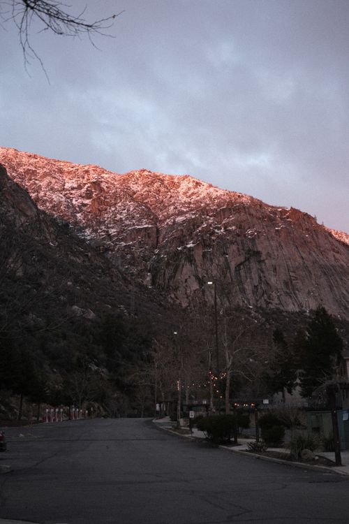 Free A serene rural road leads to a mountain with a pinkish glow at sunset, framed by trees. Stock Photo