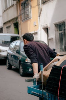 A man walks down a narrow urban street pulling a trailer, showcasing everyday city life.