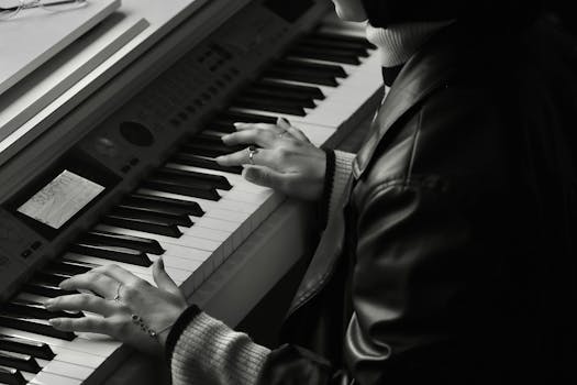 Close-up of a musician's hands playing an electronic keyboard in black and white.