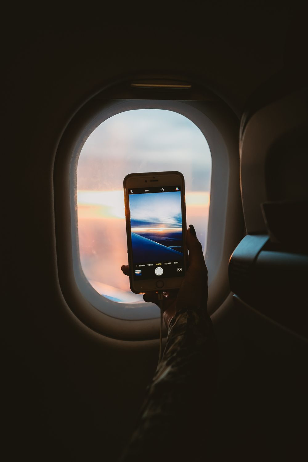Passenger photographing the sunset through an aircraft window on a smartphone