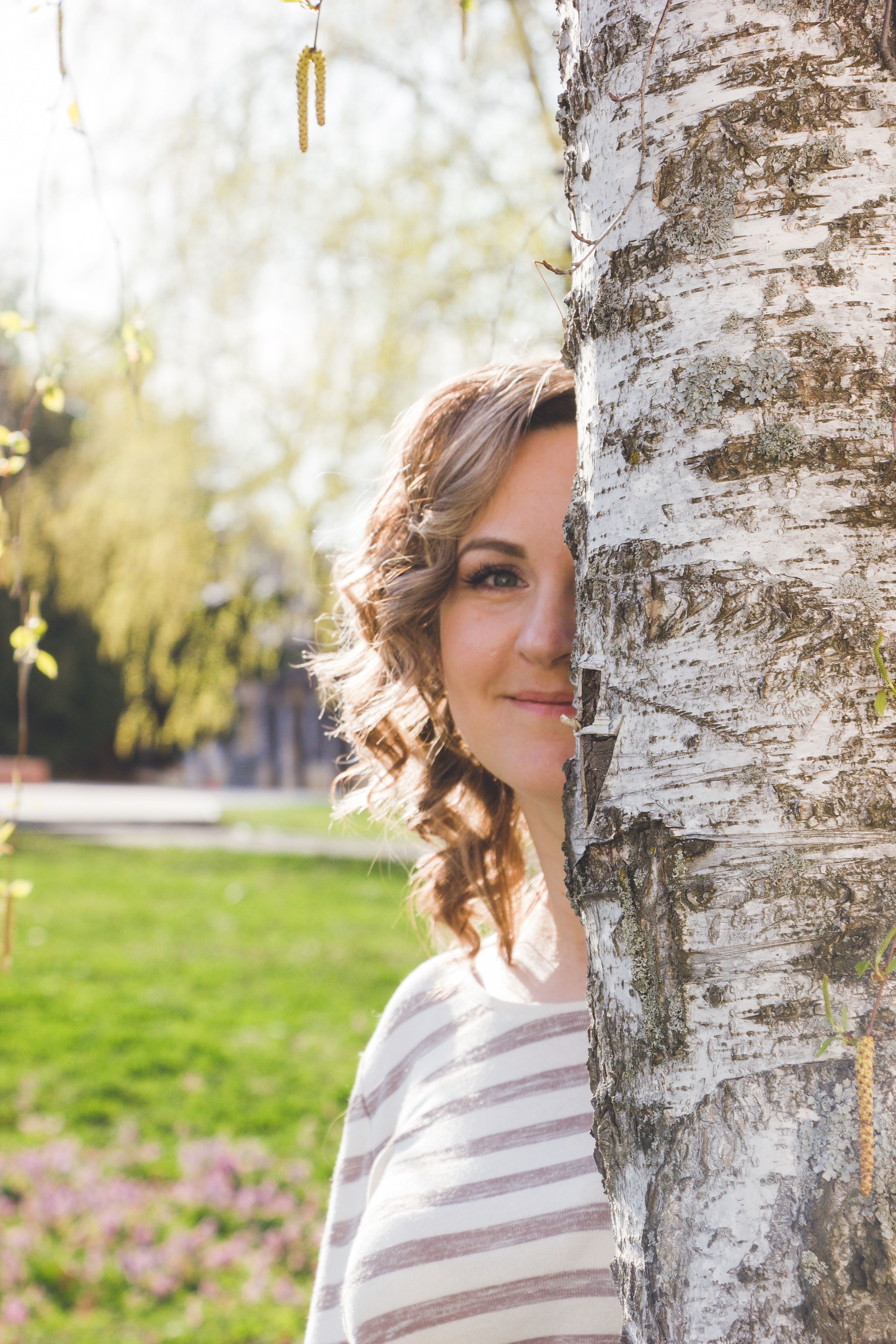 Portrait of woman hiding playfully behind a birch tree outdoors.