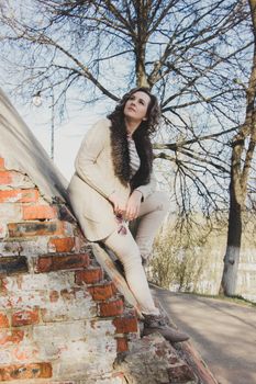 Stylish woman posing on a brick wall in an urban park setting.