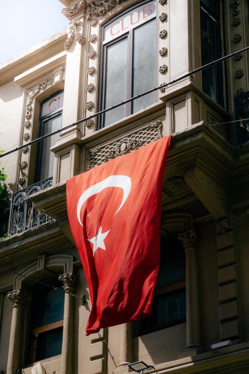 Free Red Turkish flag with white crescent and star on a historic Istanbul building facade. Stock Photo