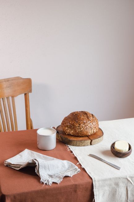 A rustic scene featuring whole grain bread, butter, and milk on a wooden table with warm textiles.
